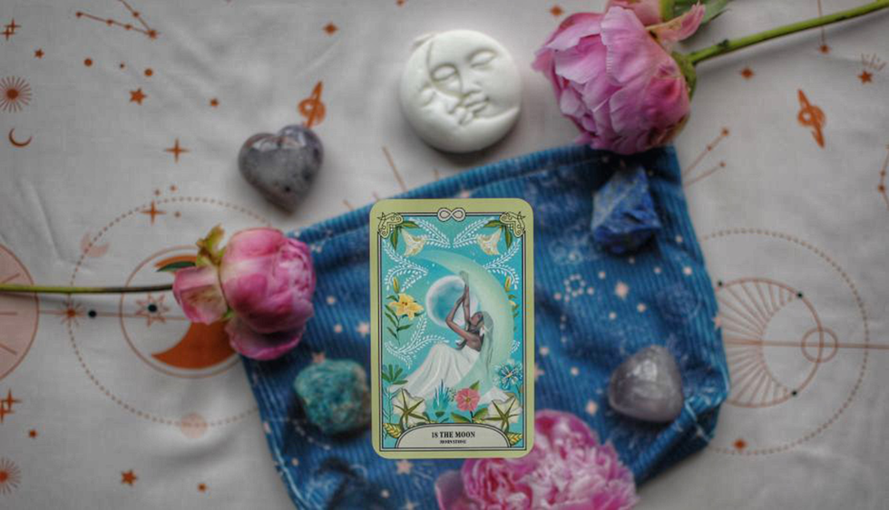 tarot card depicting a figure with a moon backdrop surrounded by natural elements and crystals